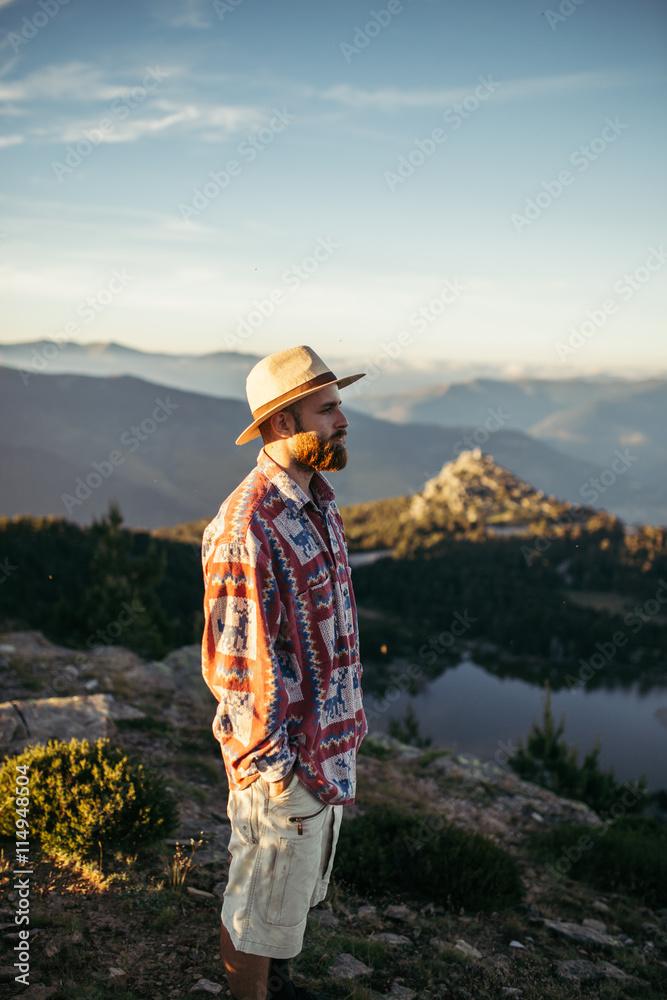Man with hat standing in  the top of a mountain with a lake