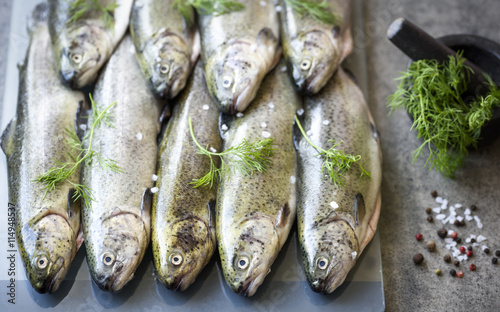 Rainbow trouts on a glass and stone board with herbs and mortar