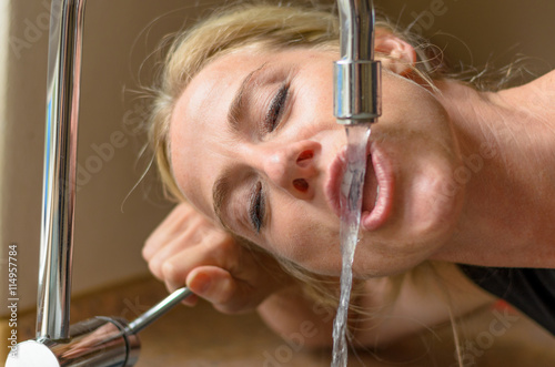 Woman drinking from a kitchen faucet
