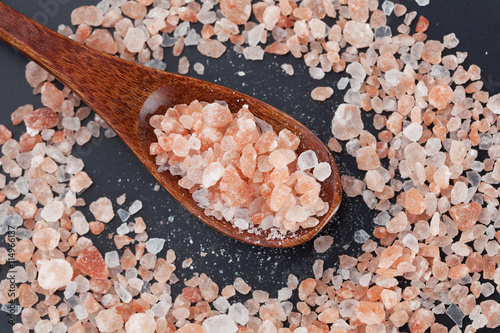 Himalayan pink rock salt in wooden spoon closeup, top view