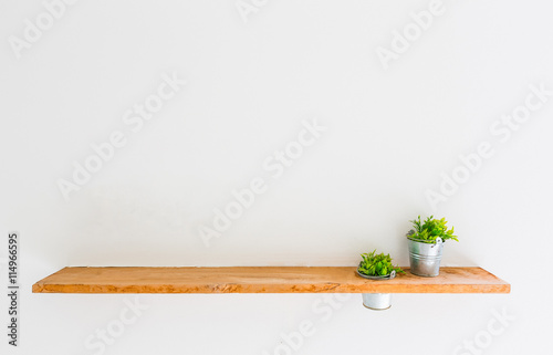 Fotótapéta Wooden shelf on white wall with green plant.