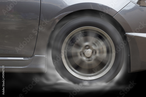Grey Car racing spinning wheel burns rubber on floor.