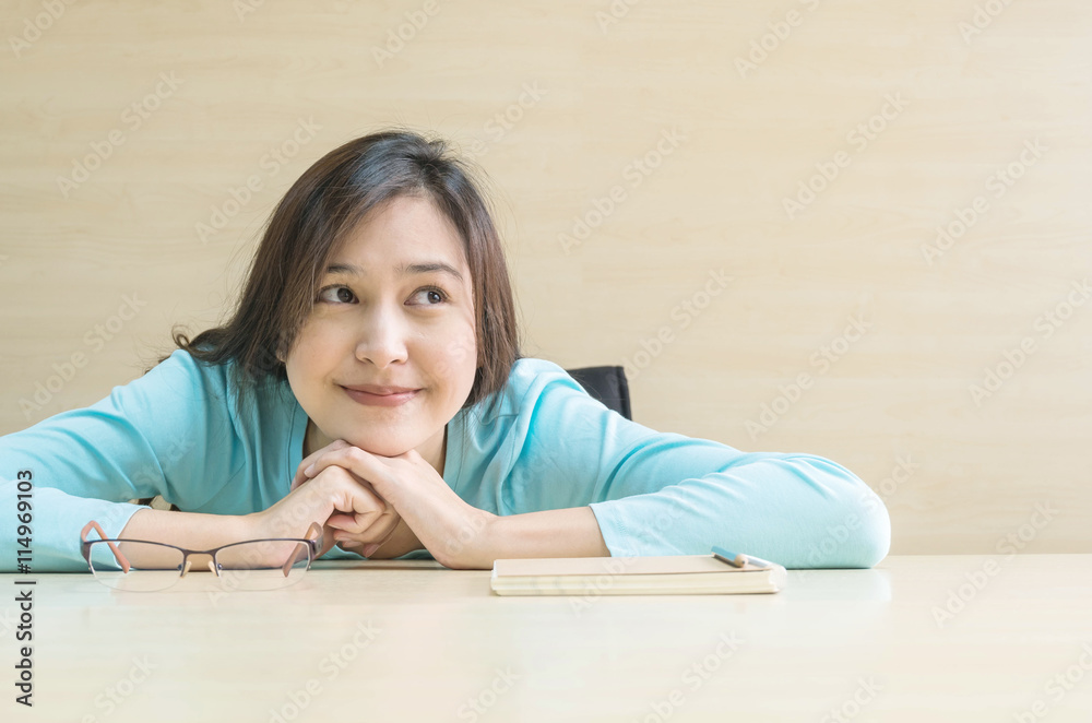 Closeup asian woman lied on desk with happy face in rest time from reading a book on blurred wooden desk and wall textured background in the meeting room , happy time and relaxation of woman concept Closeup asian woman lied on desk with happy face in rest time from reading a book on blurred wooden desk and wall textured background in the meeting room , happy time and relaxation of woman concept