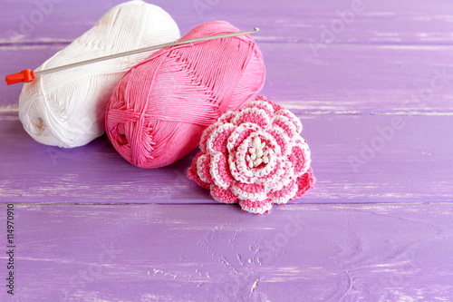 Home made pink and white crochet flower decorated with beads. Two skeins of cotton yarn and crochet hook on lilac wooden background. Easy and beautiful knitting idea 