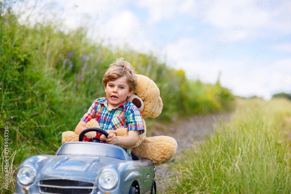 Little kid boy driving big toy car with a bear, outdoors. Little kid boy driving big toy car with a bear, outdoors.