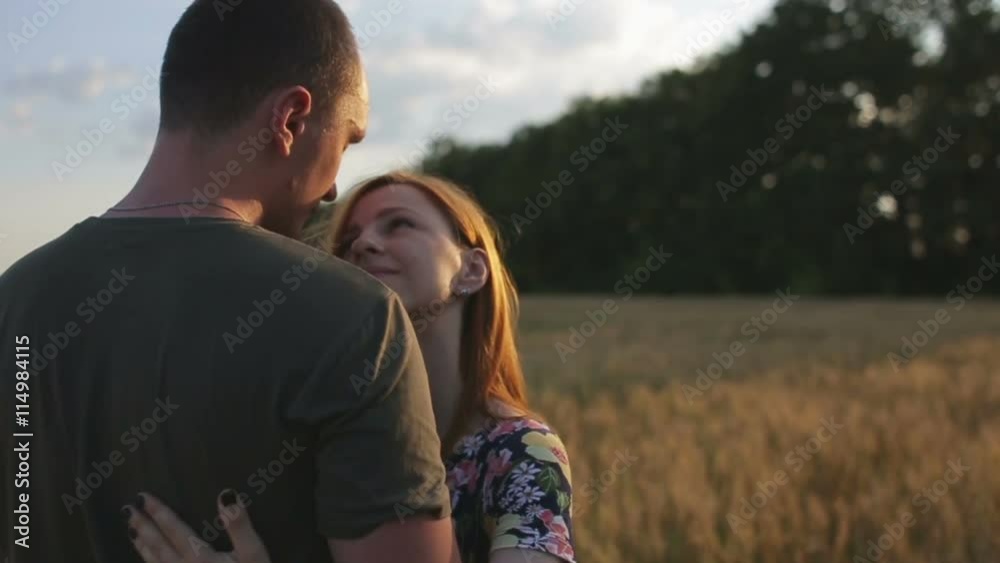 A couple hug, kiss and then walk in a wide open golden field at sunset A couple hug, kiss and then walk in a wide open golden field at sunset