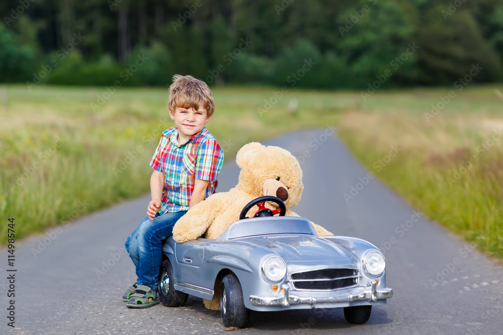 Little kid boy driving big toy car with a bear, outdoors. Little kid boy driving big toy car with a bear, outdoors.