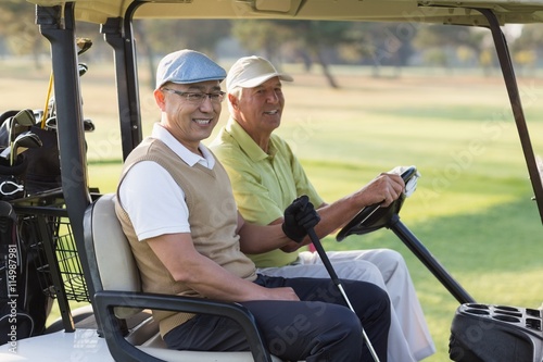 Smiling male golfer friends sitting in golf buggy 