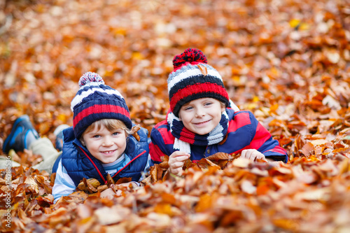Two little kid boys lying in autumn leaves  in park.