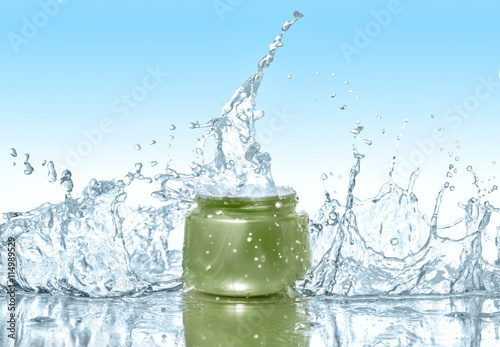 Green jar of moisturizing cream stays on the blue water background with big water splashes around