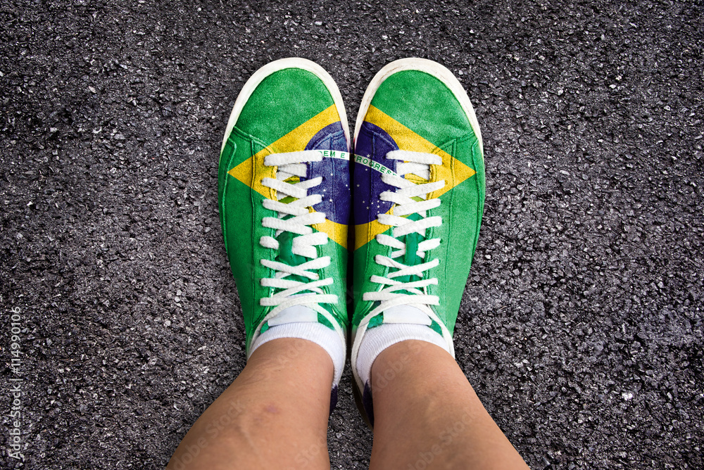 Φωτογραφία Legs wth sport shoes colored the brazilian flag, asphalt background