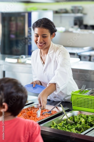 Tableau sur toile Smiling woman serving food to schoolboy