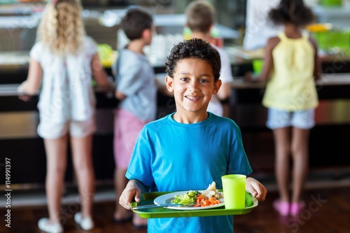 Foto Happy schoolboy holding food tray in canteen