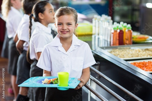 Картината върху платно Cute schoolgirl with classmate standing near canteen counter