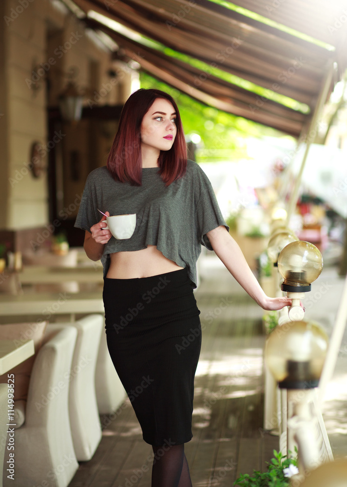 Stylish brunette with cup of coffee on background of summer cafe