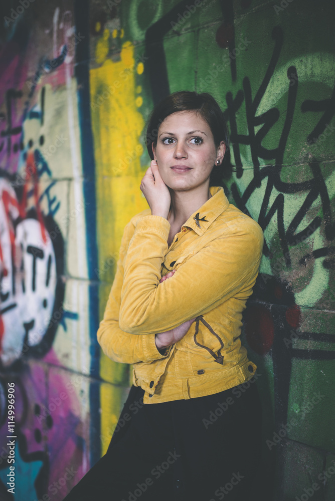 Portrait of young woman wearing yellow jacket standing in front of graffiti Portrait of young woman wearing yellow jacket standing in front of graffiti