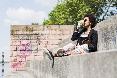 Young businesswoman with digital tablet drinking coffee to go at riverside photo