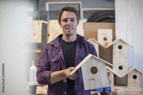 Smiling man holding self-made birdhouse in workshop photo