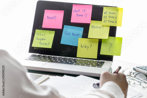 Businessman working on his desk with sticky notes with messages stuck to a laptop computer screen. Pending work concept.