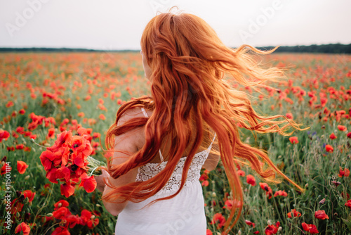 Beautiful young red-haired woman in poppy field with flying hair