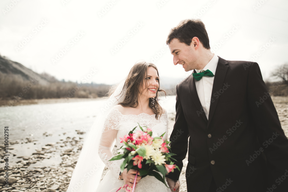 Happy wedding couple, bride and groom posing neat river against backdrop of the mountains Happy wedding couple, bride and groom posing neat river against backdrop of the mountains