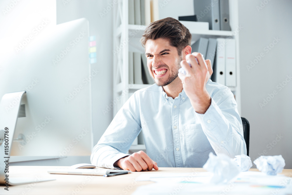 Angry businessman sitting and crumpling paper on his workplace