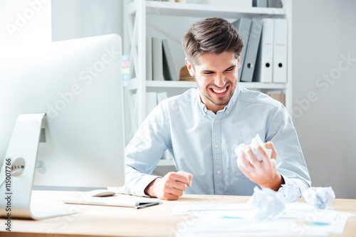 Mad annoyed businessman working and crumpling paper in office