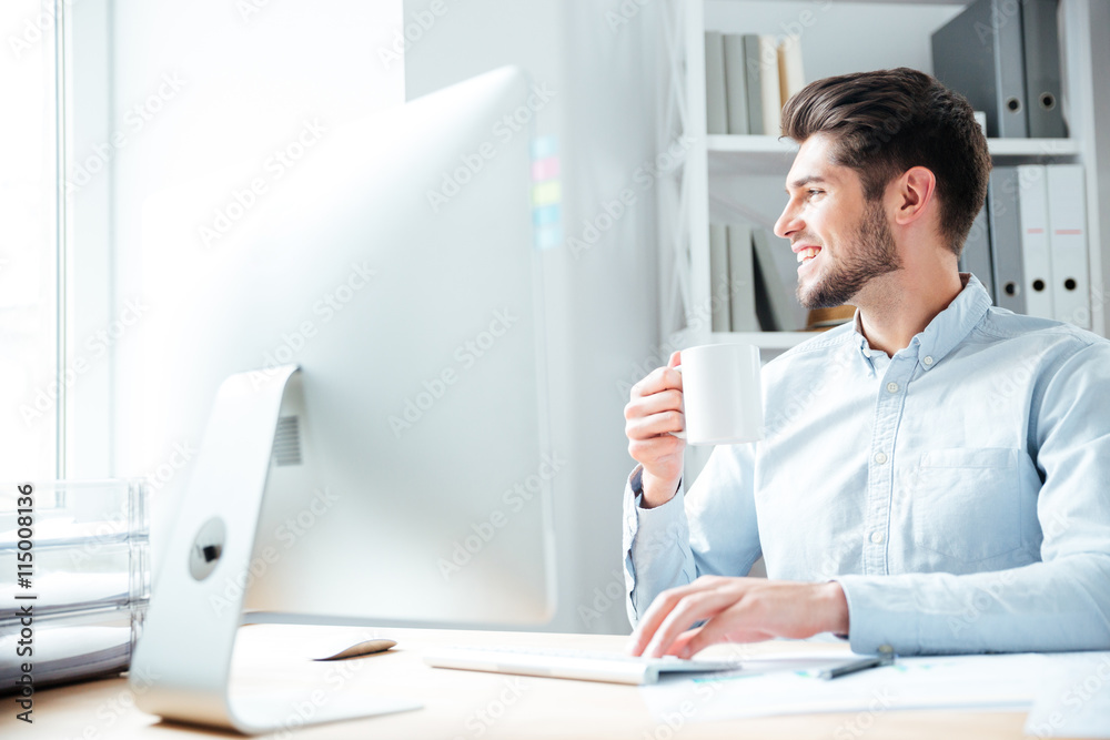 Young smiling businessman drinking coffee and looking away in office Young smiling businessman drinking coffee and looking away in office