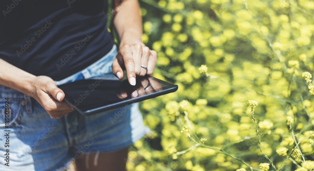 Hipster texting message on tablet or technology, mock up of blank screen. Girl using computer on yellow flowers background close.Gadget on blurred backdrop. Mockup side view. space for text message