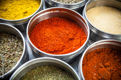 Spices and herbs in metal containers on wooden table