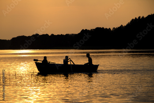 rowing wooden boat near forest in late evening during sunset
