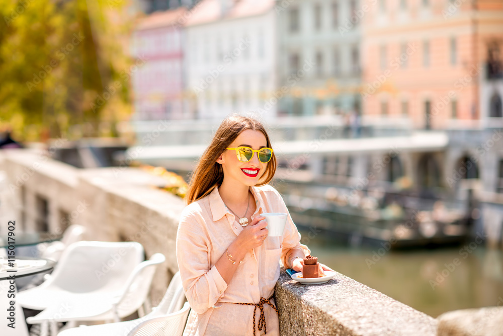 Young woman enjoying coffee with chocolate cake near the river in the center of Ljubljana city. Traveling Slovenia