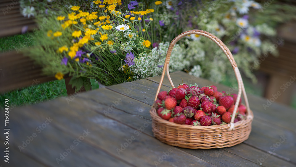 Strawberries in a wicker basket on a background of summer bouque Strawberries in a wicker basket on a background of summer bouque