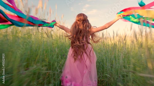Young girl running with colored ribbons in her hands through the wheat field