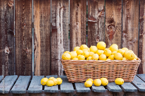 A basket of many lemons on a rustic plank table and background.