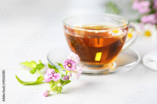 Beautiful meadow flowers and cup of tea on light background