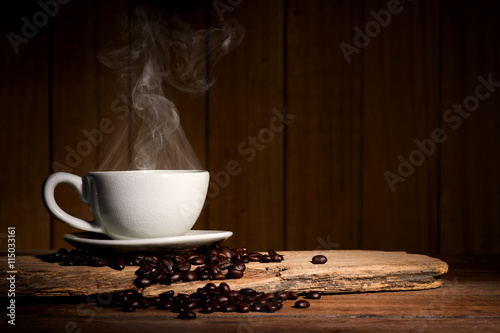 Steaming coffee cup and coffee beans on wood background with copy-space and dark tone.