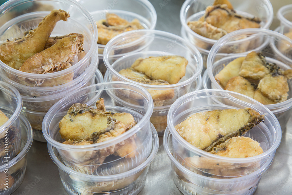 Preparing fried fish in plastic food package for take away Preparing fried fish in plastic food package for take away