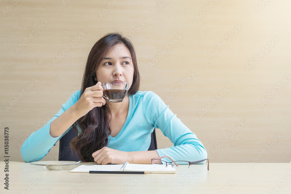 Working woman sit for drinking coffee in cup of coffee with thinking emotion in relax time on wood desk and wood wall textured background in meeting room , coffee break of working woman concept Working woman sit for drinking coffee in cup of coffee with thinking emotion in relax time on wood desk and wood wall textured background in meeting room , coffee break of working woman concept