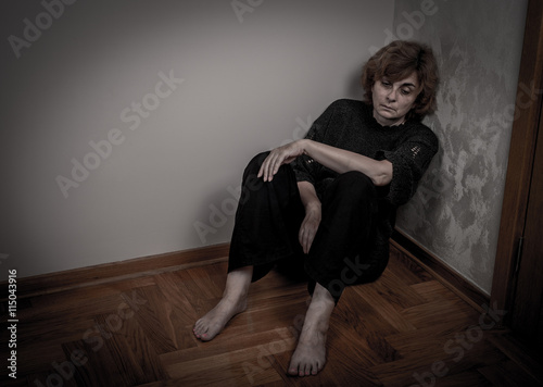 Depressed and sad woman sitting on the floor in the empty room. Low key.