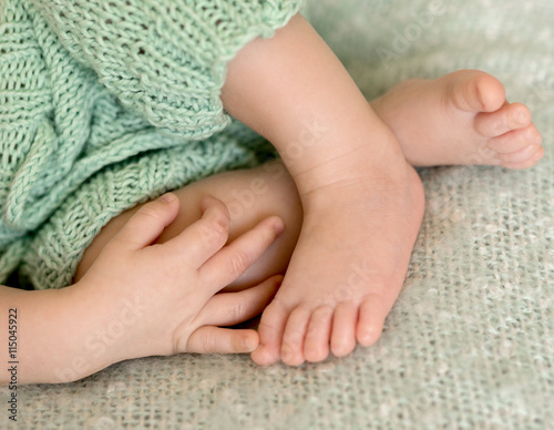 lovely tiny crossed baby legs out of pants and hand on them, closeup
