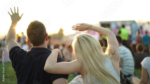4k footage, back view young couple enjoying summer music festival at sunset, crowd and stage blurred

