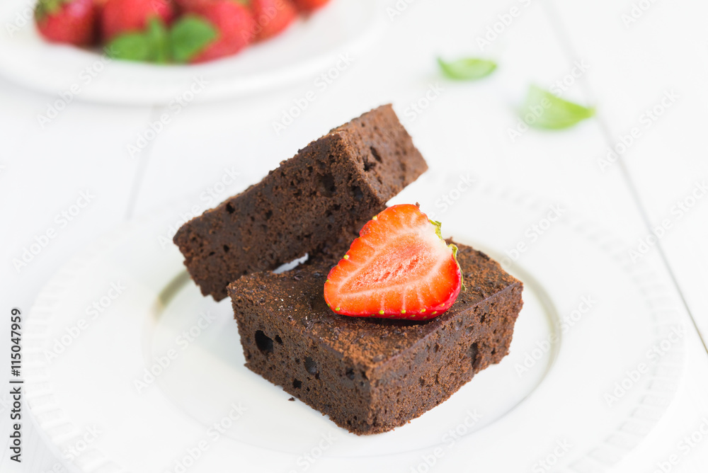 Chocolate brownie cake on white plate decorated with strawberrie