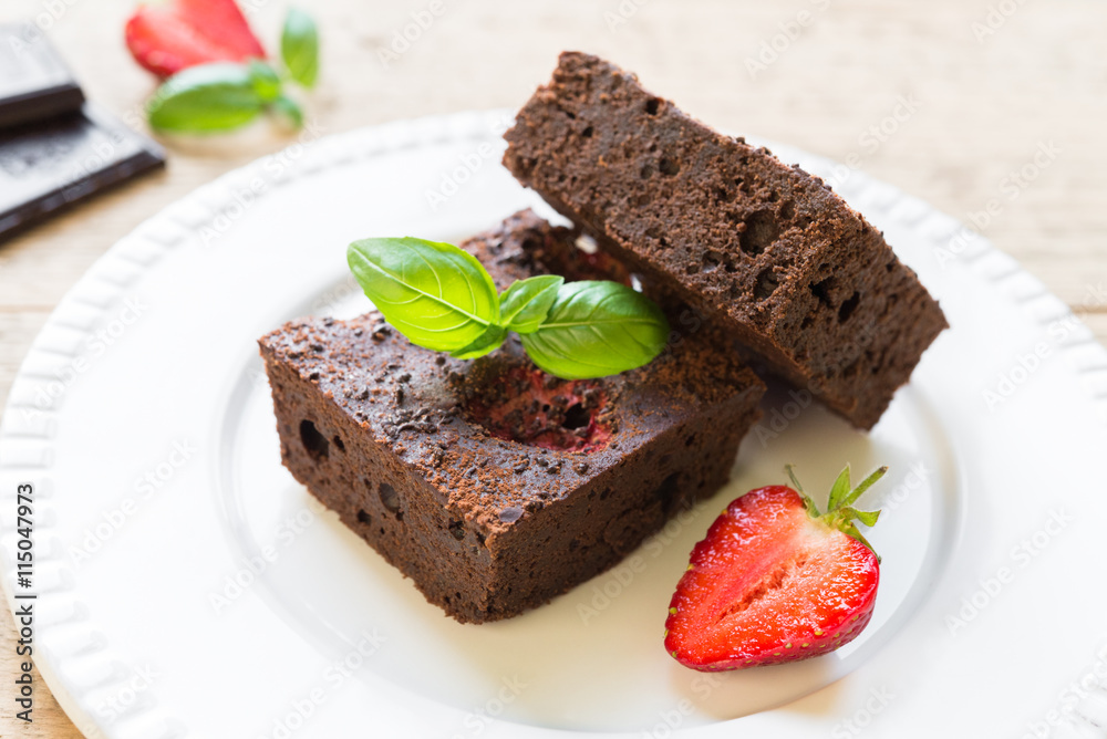 Chocolate brownie cake on white plate decorated with strawberrie