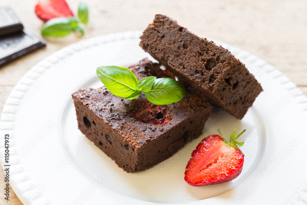 Chocolate brownie cake on white plate decorated with strawberrie Chocolate brownie cake on white plate decorated with strawberrie