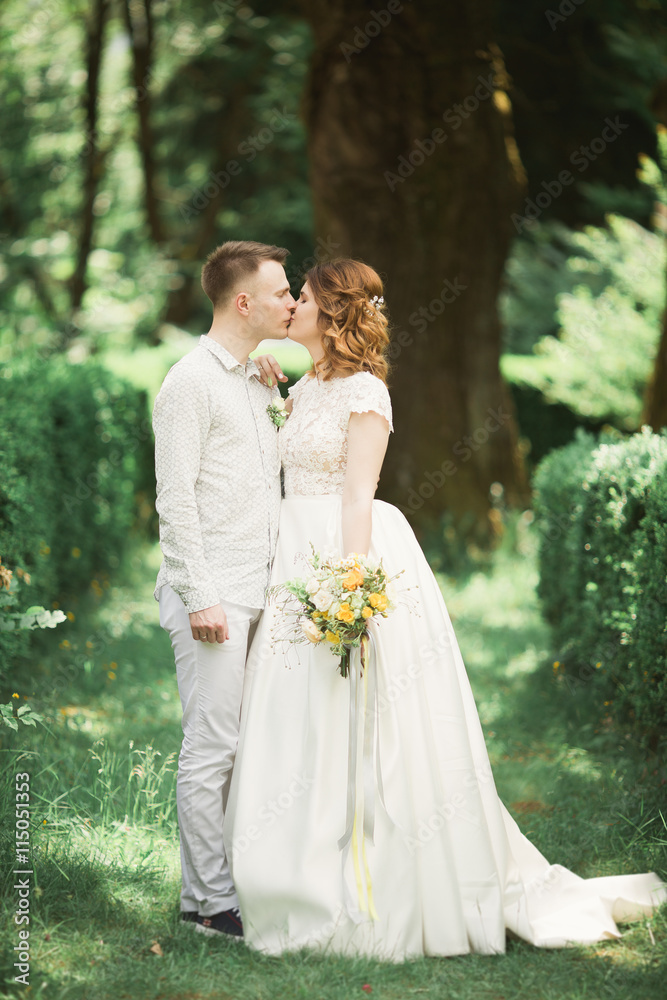 Stylish couple of happy newlyweds walking in the park on their wedding day with bouquet Stylish couple of happy newlyweds walking in the park on their wedding day with bouquet