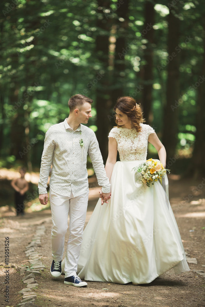 Stylish couple of happy newlyweds walking in the park on their wedding day with bouquet Stylish couple of happy newlyweds walking in the park on their wedding day with bouquet