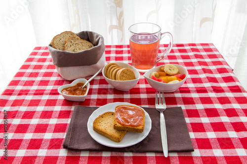 Fette biscottate con marmellata, te, frutta, biscotti e pane su tovaglia a quadri rossi e bianchi