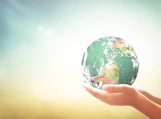 Child hands holding glass globe over blurred green nature background