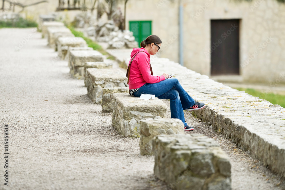 Brunette woman sitting on stone bench in garden texting on smart
